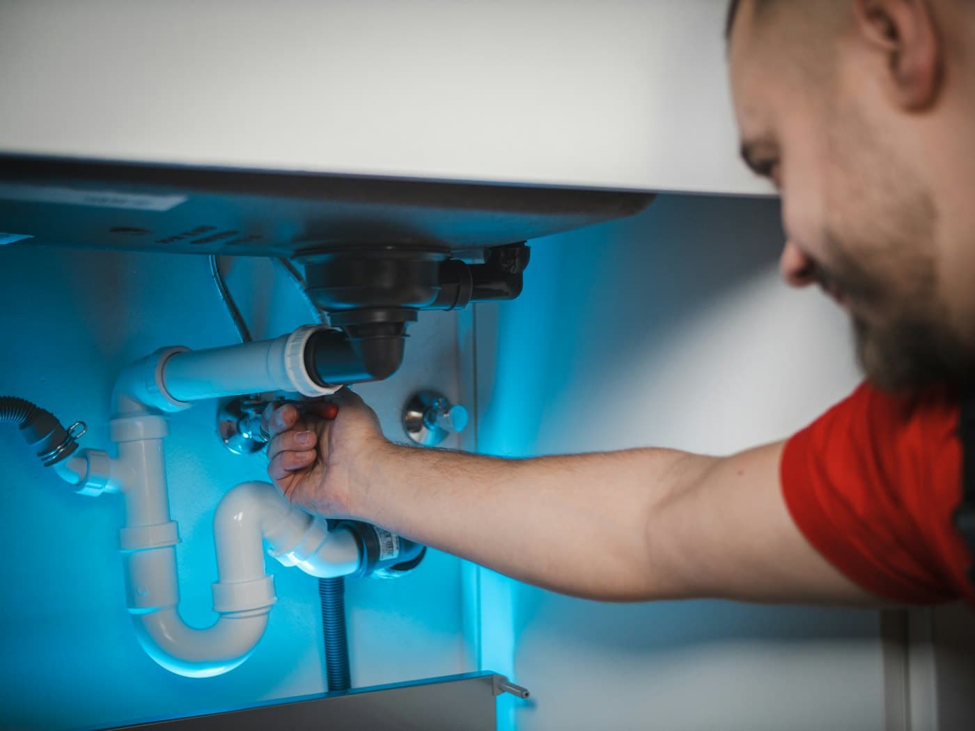 A Fall Creek technician tightening a drain trap under a kitchen sink